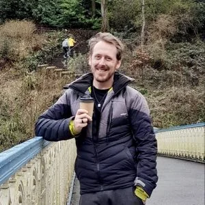 Simon Archer holding a coffee on a footbridge